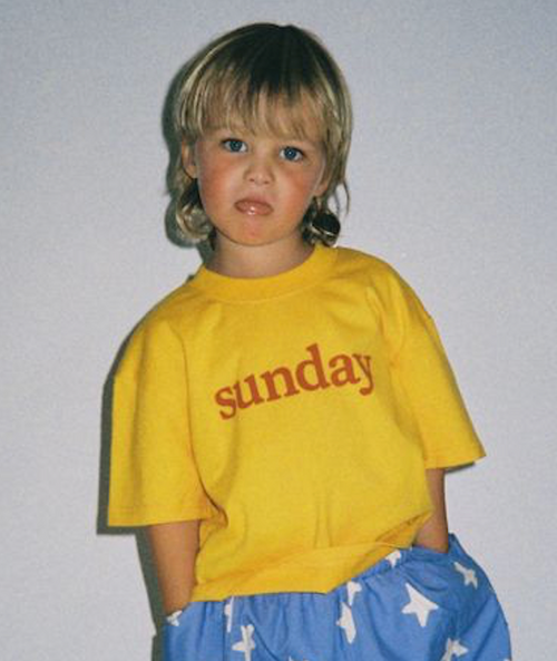 Child wearing a yellow shirt with 'sunday' printed on it against a plain background